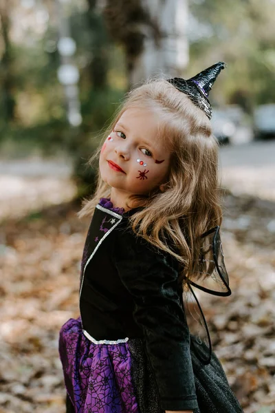 Cadılar Bayramı 'nda cadılar bayramı için siyah kostümlü küçük kız asaya bakıyor. — Stok fotoğraf