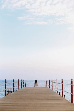 Kız iskelede oturup ve deniz ufuk ve mavi gökyüzüne bakıyor. Denizde tatil. Yaz saati deniz tatil arka plan 
