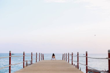 Kız iskelede oturup ve deniz ufuk ve mavi gökyüzüne bakıyor. Denizde tatil. Yaz saati deniz tatil arka plan 