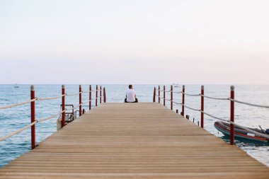 İskelede oturup ve deniz ufuk ve mavi gökyüzüne bakarak dostum. Denizde tatil. Yaz saati deniz tatil arka plan 