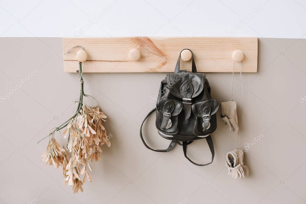Interior details of children's room on light background. Decorative wooden hanger with bag on white and brown wall as detail of kid interior. 