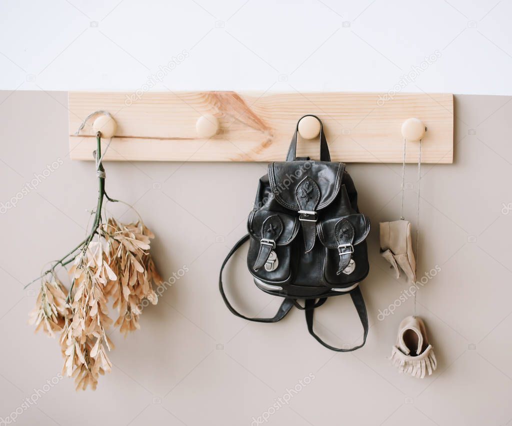 Interior details of children's room on light background. Decorative wooden hanger with bag on white and brown wall as detail of kid interior. 