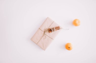 Hediye kutusu tarçın ve beyaz zemin üzerine mandalina ile dekore edilmiştir. Yılbaşı yeni yıl en az şenlikli tatil kompozisyon. Flatlay, üstten görünüm.