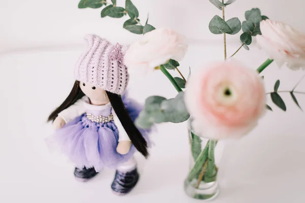 Cute doll  and a bouquet of spring flowers on white background. Handmade doll in a dress.