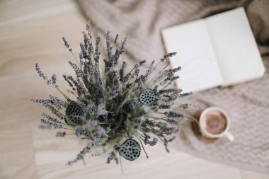 ahşap arka planda kitap ve fincan kahve ile lavanta buket. Kurutulmuş çiçekler ve kitap ile bir fincan cappuccino, bahar konsepti. üst görünüm. yatık
