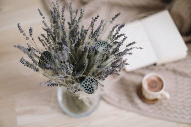 ahşap arka planda kitap ve fincan kahve ile lavanta buket. Kurutulmuş çiçekler ve kitap ile bir fincan cappuccino, bahar konsepti. üst görünüm. yatık