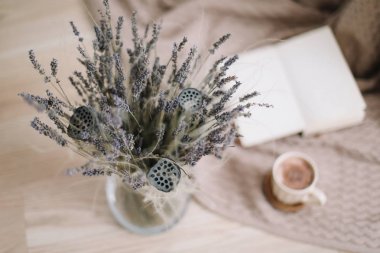 ahşap arka planda kitap ve fincan kahve ile lavanta buket. Kurutulmuş çiçekler ve kitap ile bir fincan cappuccino, bahar konsepti. üst görünüm. yatık