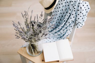 Yaratıcı düz üst görünümü yatıyordu. Mavi elbise, güneş şapkası, vazoda çiçekler ve ahşap arka plan üzerine bir kitap. Yaz tatili konsepti. Romantik duvar kağıdı