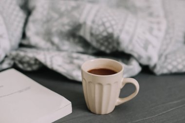 Yün bej kazak, sıcak örgü ekose, bir kitap ve kahve fincanı. Yatakta kahvaltı. Eviniz güzelmiş. düz, durgun hayat