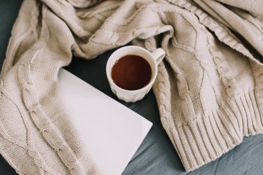 Yün bej kazak, sıcak örgü ekose, bir kitap ve kahve fincanı. Yatakta kahvaltı. Eviniz güzelmiş. düz, durgun hayat