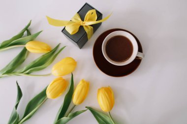 Bir fincan kahve, bir hediye kutusu ve beyaz arka planda laleler. Düz döşeme, üst görünüm, kopyalama alanı