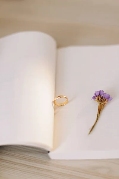 An engagement ring on the background of a book and a flower. Proposal of marriage. Wedding details.