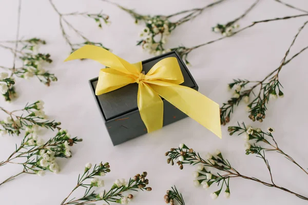 Una caja de regalo enmarcada por ramas y hojas sobre fondo blanco. Asiento plano, vista superior. Concepto de fiesta, cumpleaños, Pascua, 8 de marzo . — Foto de Stock