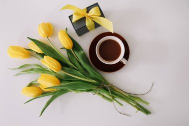 Kahve fincanı, kurdeleli bir hediye kutusu ve beyaz arka planda izole edilmiş sarı lale buketi. Düz döşeme, üst görünüm, kopyalama alanı