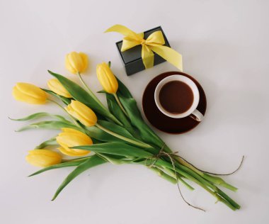 Kahve fincanı, kurdeleli bir hediye kutusu ve beyaz arka planda izole edilmiş sarı lale buketi. Düz döşeme, üst görünüm, kopyalama alanı