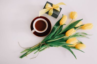 Kahve fincanı, kurdeleli bir hediye kutusu ve beyaz arka planda izole edilmiş sarı lale buketi. Düz döşeme, üst görünüm, kopyalama alanı