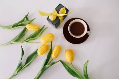 Kahve fincanı, kurdeleli bir hediye kutusu ve beyaz arka planda izole edilmiş sarı lale buketi. Düz döşeme, üst görünüm, kopyalama alanı