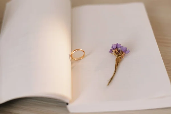 Un anillo de compromiso en el fondo de un libro y una flor. Propuesta de matrimonio. Detalles de boda . — Foto de Stock