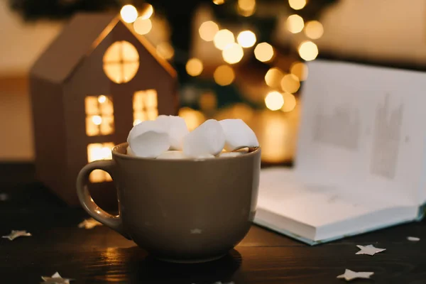 Tazza di caffè con marshmallow e un libro sul tavolo. Natura morta su sfondo scuro . — Foto Stock