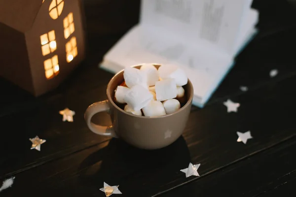 Tazza di caffè con marshmallow e un libro sul tavolo. Natura morta su sfondo scuro . — Foto Stock