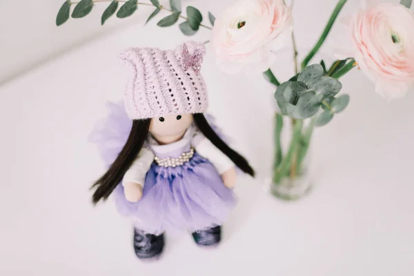 Cute doll  and a bouquet of spring flowers on white background. Handmade doll in a dress.