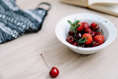 En iyi görünüm seyahat veya tatil konsepti. Mayo, şapka, kitap ve ahşap arka plan üzerinde taze tatlı kiraz ve çilek. Düzlay. Yaz arka planı. 