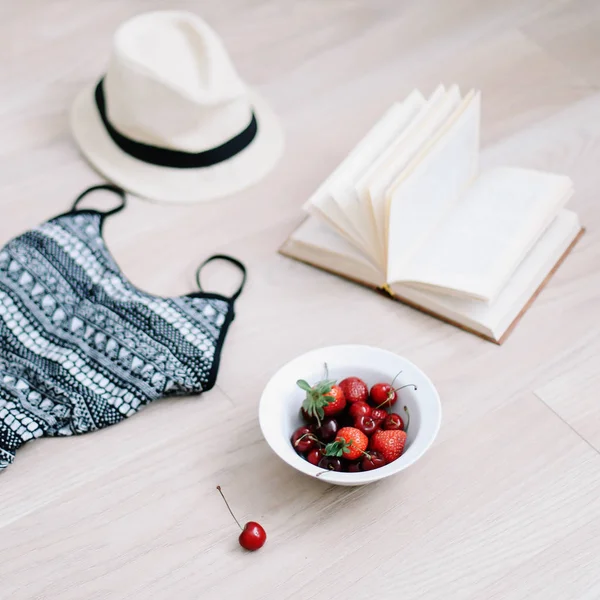 Top vista viagem ou férias conceito. Fato de banho, chapéu, livro e cerejas doces frescas e morangos em fundo de madeira. Flatlay. Fundo de verão . — Fotografia de Stock