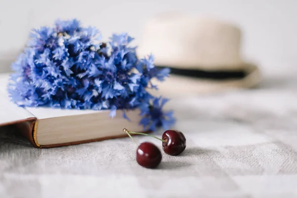 Čerstvé třešně, cornflowerky, slaměný klobouk a knížka na stole. Letní plochá Tapeta, pohled shora — Stock fotografie