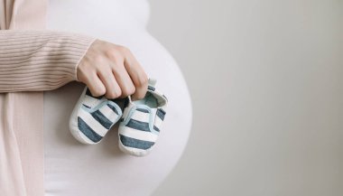Müstakbel bir annenin elinde patikler. Hamile göbek yakın çekim. Hamilelik ve doğum konsepti. Bebek duş
