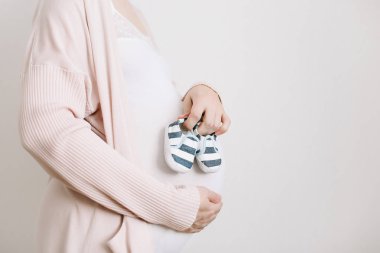 Müstakbel bir annenin elinde patikler. Hamile göbek yakın çekim. Hamilelik ve doğum konsepti. Bebek duş