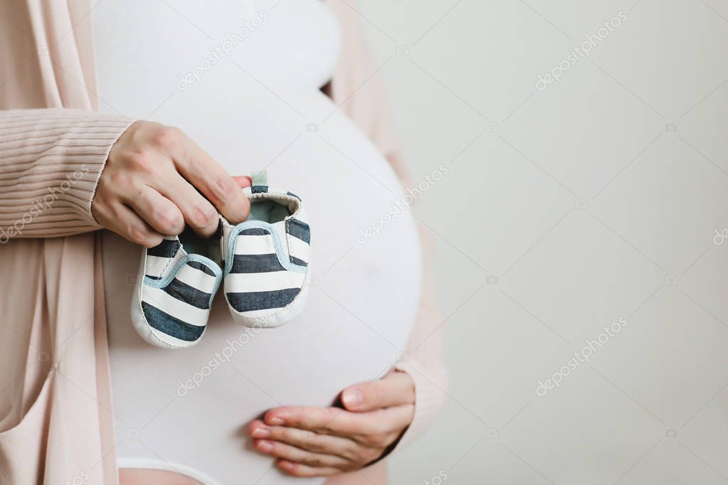 Pregnant mother holding Baby booties in hands above belly. Healthy pregnancy