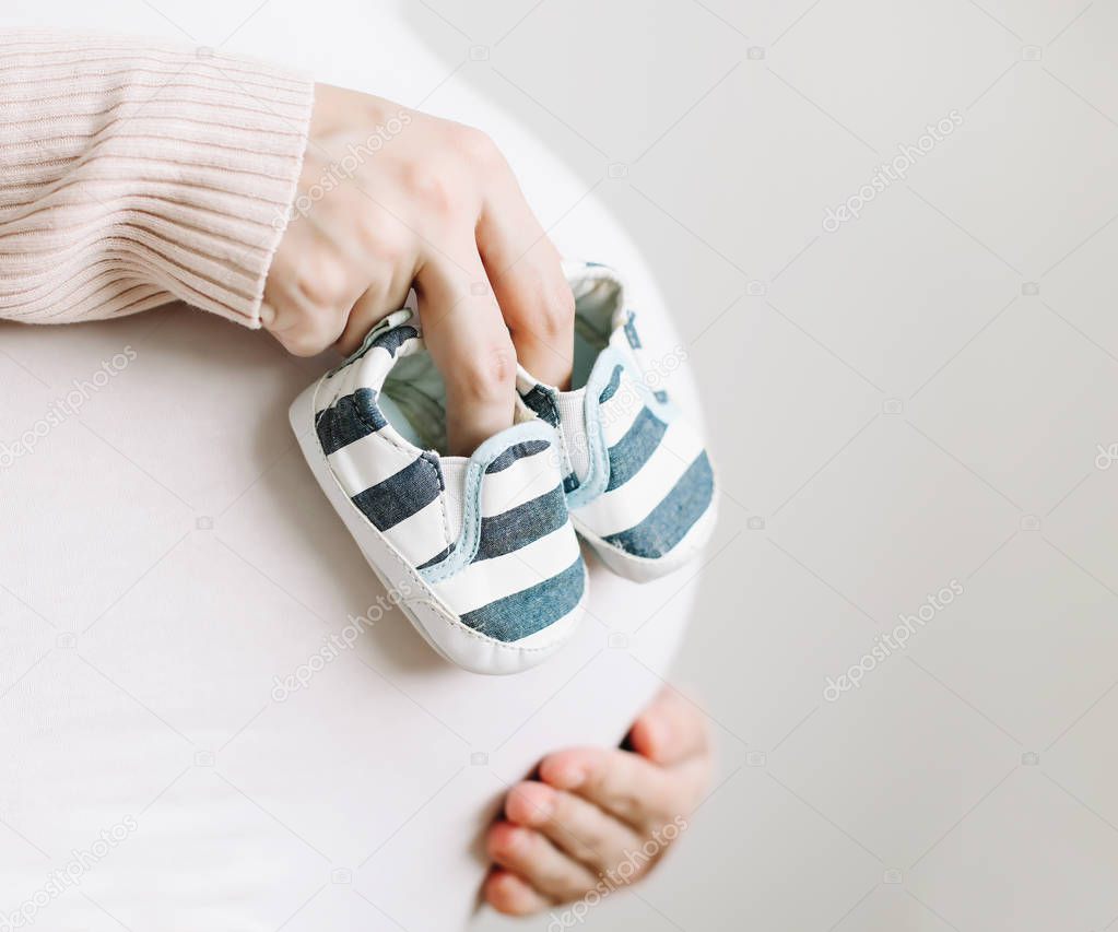 Baby shoes on the belly of a pregnant woman. Mother touching belly. A woman waiting for baby. 