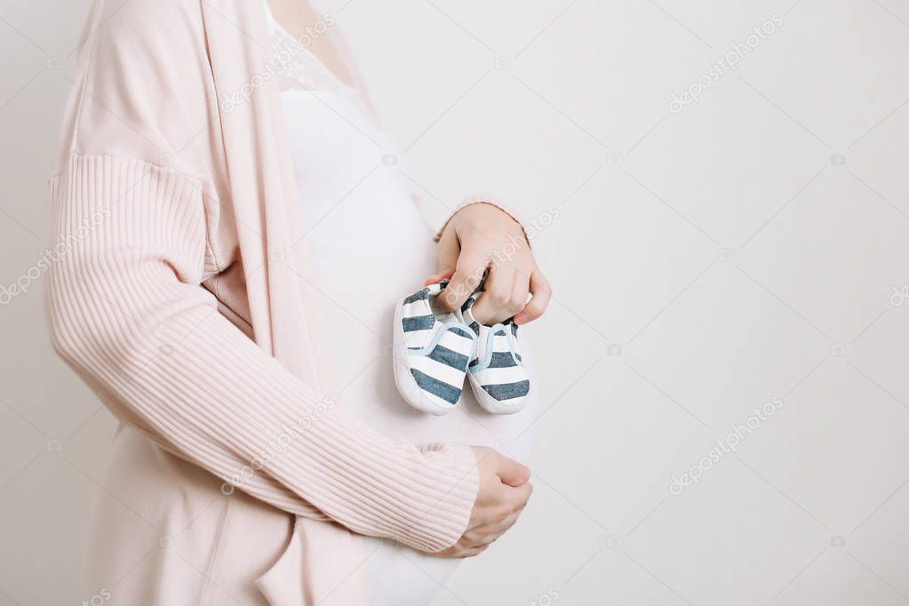 Booties in the hands of a future mother. Pregnant belly closeup. Pregnancy and maternity concept. Baby shower