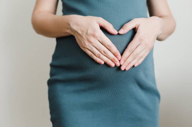 Elbiseli hamile kadını karnından beyaz bir arka plan üzerinde ellerini tutar. Gebelik, hamile, hazırlık ve beklenti kavramı. 