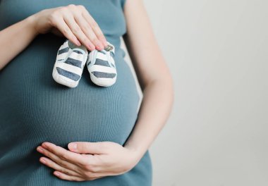 Anne, yeni doğan bebek için ayakkabı tutuyor. Hamile kadın karnına dokunuyor. Mutlu kadın gebelik, annelik, vücut bakımı