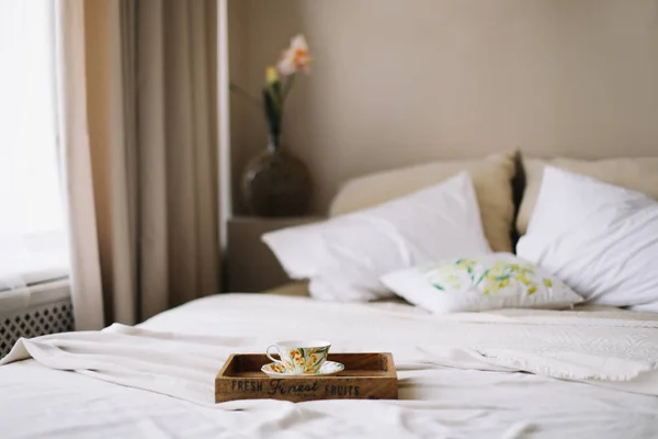 Breakfast in bed. Wooden tray with coffee cup. Bed with bedspread, white sheets and pillows and a cup. White bedroom.  flat lay — Stock Photo, Image