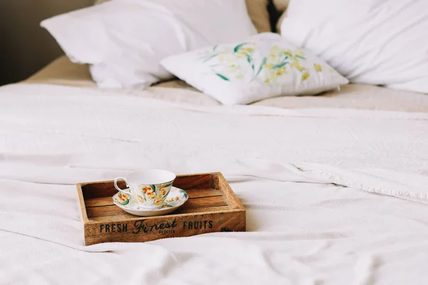 Colazione a letto. Vassoio in legno con tazza di caffè. Letto con copriletto, lenzuola e cuscini bianchi e una tazza. Camera bianca. posa piatta — Foto Stock