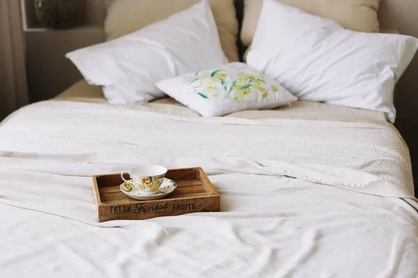 Breakfast in bed. Wooden tray with coffee cup. Bed with bedspread, white sheets and pillows and a cup. White bedroom.  flat lay — Stock Photo, Image