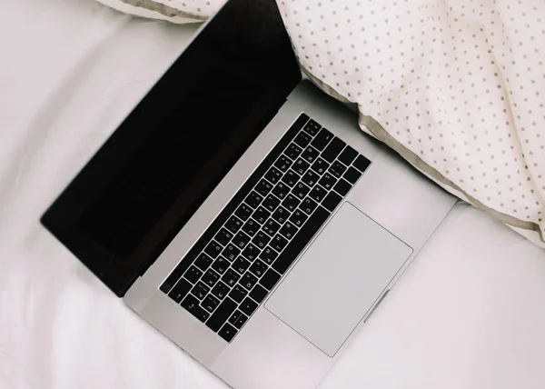 Laptop in bed on white linens. Work at home concept.  Flat lay, top view, lifestyle, minimalist workspace background.