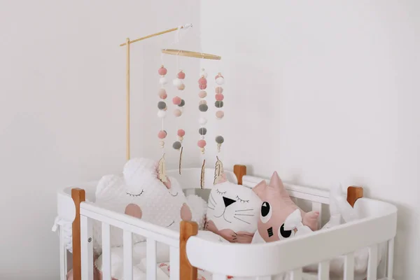Hermoso interior de la habitación del bebé. Cuna blanca con almohadas y manta rosa en la habitación del bebé. ropa de cama rosa en la cama contra la pared blanca —  Fotos de Stock