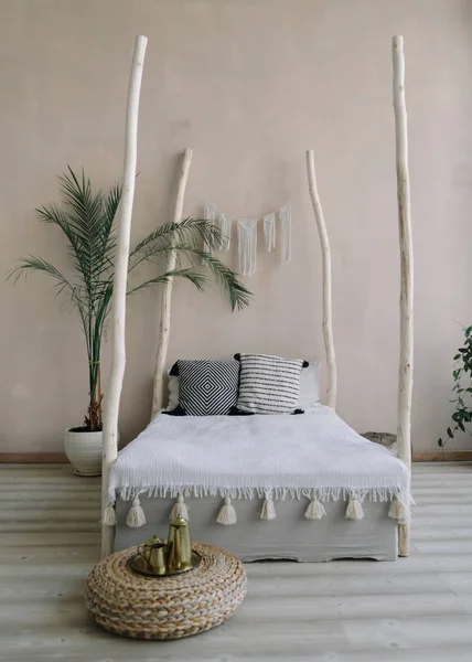 Modern minimal home interior design. Bed with wooden canopy and pillows, blanket, tropical palm. Exotic bedroom interior, scandinavian style