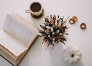 Çalışma alanı ya da ofis masasının en üst görüntüsü. Beyaz arka planda bir fincan kahve, kitap ve kurumuş çiçekler. Düz yatış, üst görünüm