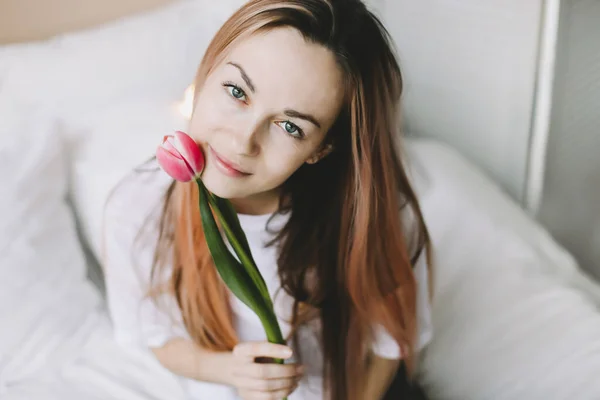 Retrato romântico de uma menina na cama com flores naturais. Menina bonita nova com buquê. Menina com buquê de tulipas rosa — Fotografia de Stock