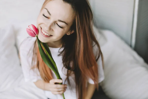 Retrato romântico de uma menina na cama com flores naturais. Menina bonita nova com buquê. Menina com buquê de tulipas rosa — Fotografia de Stock