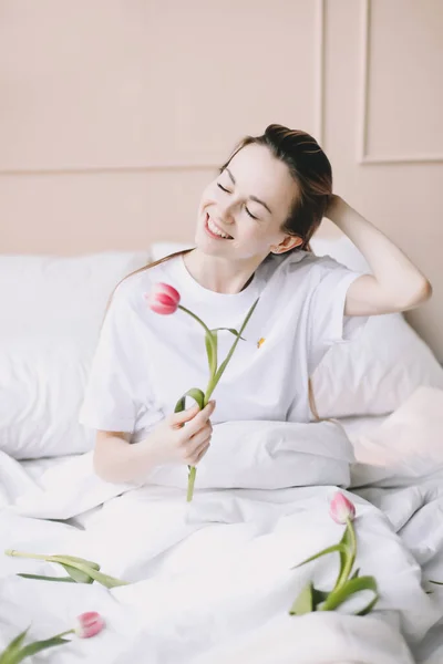 Menina romântica. Retrato de uma menina na cama com flores naturais. Jovem sonhadora com tulipas rosa descansando no quarto de manhã — Fotografia de Stock