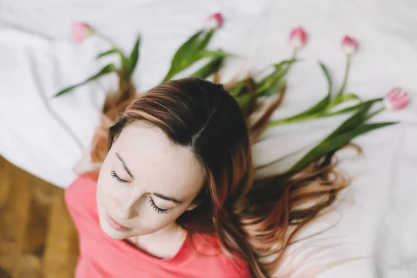 Penteado com flores. Retrato romântico de uma menina na cama com flores naturais. Jovem com tulipas no cabelo. Bela foto — Fotografia de Stock