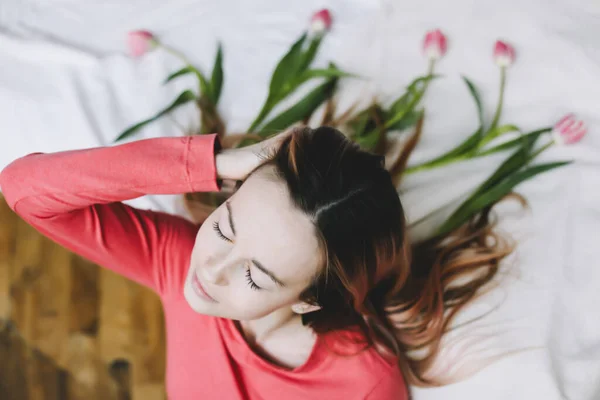 Penteado com flores. Retrato romântico de uma menina na cama com flores naturais. Jovem com tulipas no cabelo. Bela foto — Fotografia de Stock