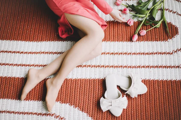 Imagen de cerca de hermosas piernas de mujer. Patas de mujer bronceadas cerca de flores y zapatillas. Foto aérea interior de una chica —  Fotos de Stock