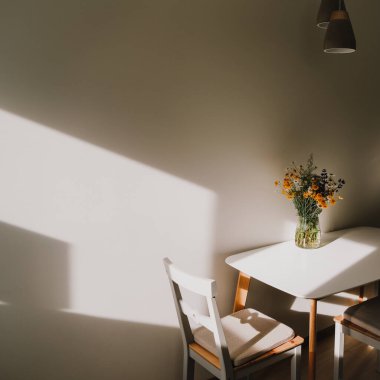 Modern yemek odası. Çiçekler ve sandalyelerle dolu beyaz bir masa. Mutfağın içi sıcacık. Evde güneşli bir sabah
