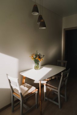Modern yemek odası. Çiçekler ve sandalyelerle dolu beyaz bir masa. Mutfağın içi sıcacık. Evde güneşli bir sabah